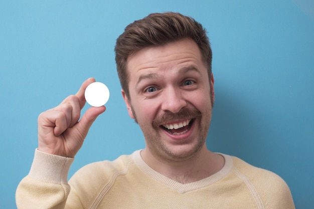 Homme avec moustache regarde la caméra tenant dans les doigts cercle blanc comme espace de copie
