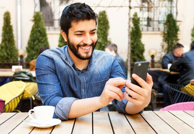 Homme multiculturel discutant avec un smartphone tout en buvant du café au café en plein air