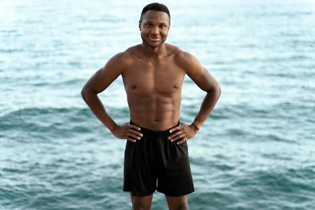 Homme multiracial gai posant avec le torse nu avec la mer d'été avec de l'eau bleue