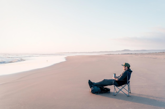 Homme mûr assis sur le rivage de la plage détendu et calme en regardant l'horizon au coucher du soleil