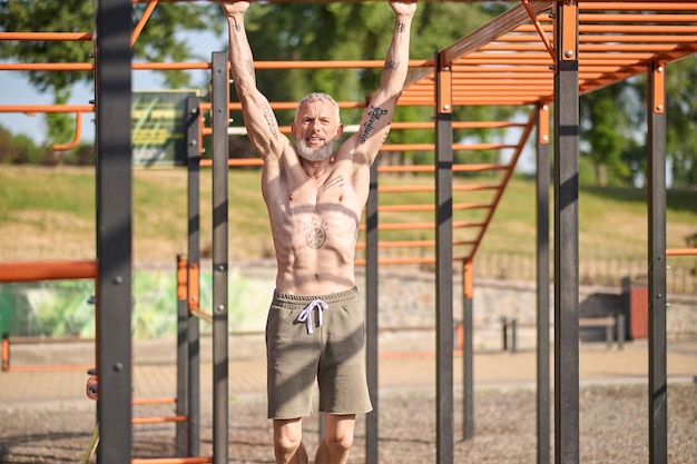 Un homme mûr aux cheveux gris ayant une séance d'entraînement sur le terrain de sport ouvert