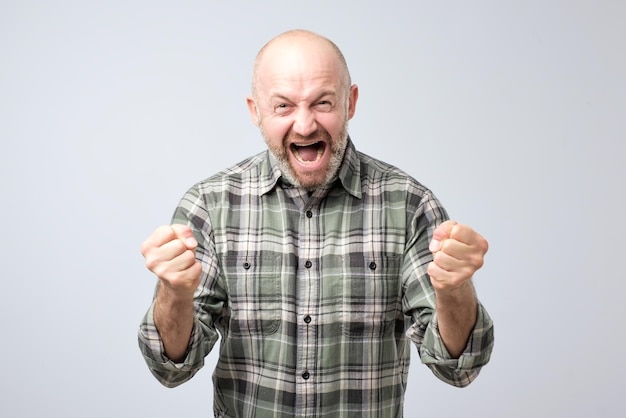 Homme mûr avec barbe célébrant la victoire sur fond gris