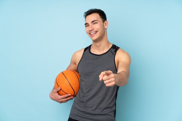 Homme sur mur bleu isolé jouant au basket-ball et pointant vers l'avant