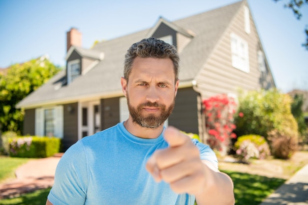 Homme mûr debout en plein air à la maison pointant le doigt sur la location de caméra