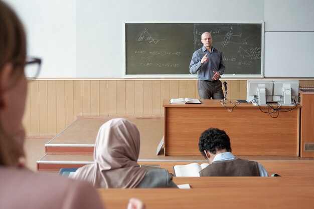 Homme mûr debout près du tableau noir pendant l'explication du sujet aux étudiants