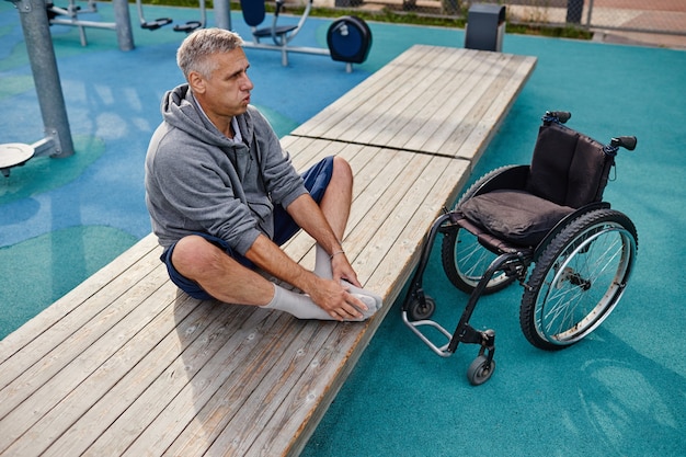 Homme mûr handicapé assis sur le banc et faisant des exercices de respiration tout en s'entraînant à l'extérieur
