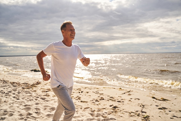 Un homme mûr heureux profite d'un entraînement cardio en plein air en courant le long du bord de mer