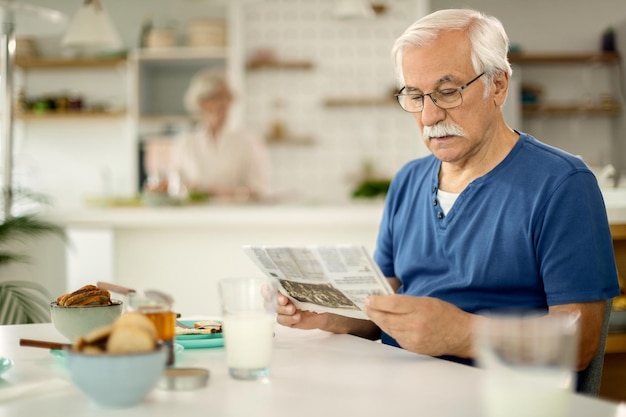 Homme mûr lisant le journal tout en prenant son petit déjeuner à la maison