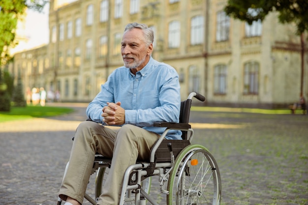 Homme mûr pensif en convalescence en fauteuil roulant à l'écart tout en passant du temps seul dans le parc près