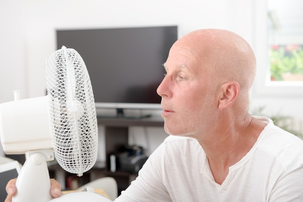 Homme mûr rafraîchi avec un ventilateur