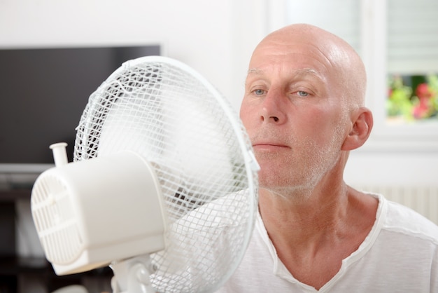 Homme mûr rafraîchi avec un ventilateur