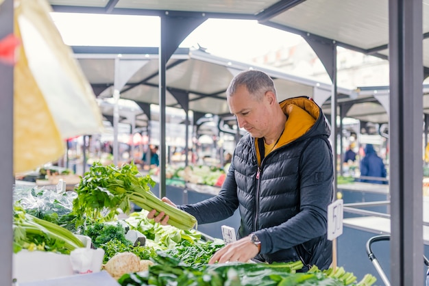 Homme mûr ramasser des légumes au marché des agriculteurs.