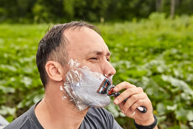 Homme mûr se rase à l'extérieur à l'aide de mousse à raser et d'un rasoir.