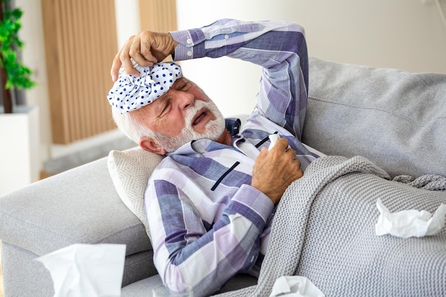 Homme mûr se sentant malade du froid et de la fièvre à la maison malade de la grippe assis sur le canapé avec un sac de glace sur la tête