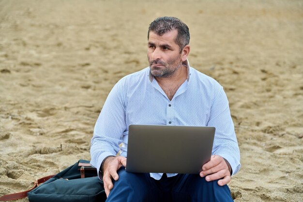 Homme mûr sérieux et confiant avec un ordinateur portable à l'extérieur