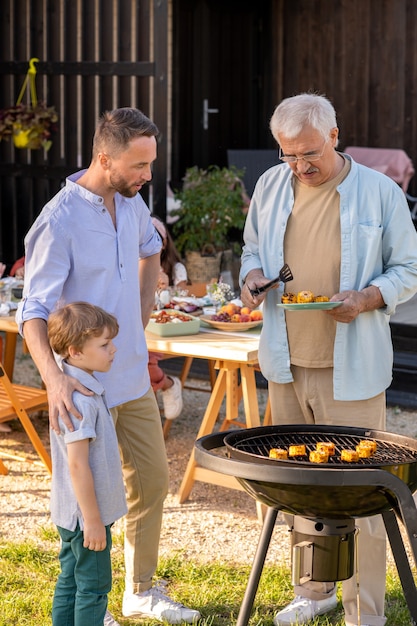 Homme mûr son fils et petit-fils faisant du maïs grillé pour le dîner de famille