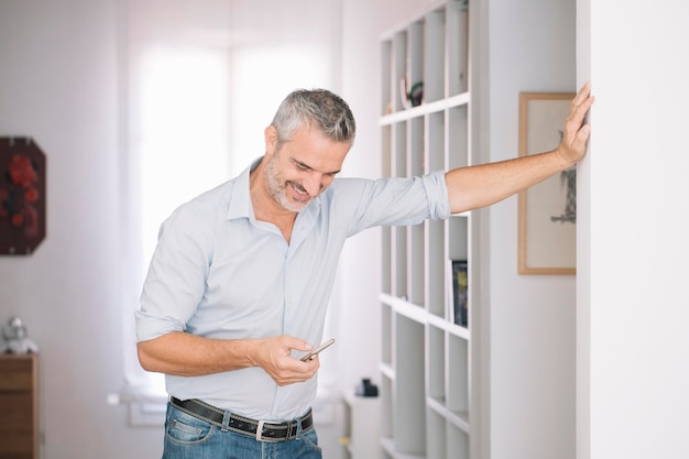 Homme mûr souriant utilisant un téléphone portable à la maison