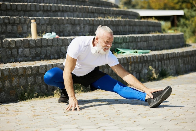 Homme mûr sportif en tenue de sport s'entraînant à l'extérieur par une journée ensoleillée faisant des exercices d'étirement des jambes