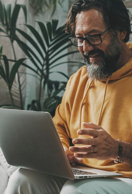 Homme mûr travaillant sur un ordinateur portable à la maison assis sur le canapé Technologie moderne loisirs activité intérieure En ligne les gens occupés sur l'appel vidéo avec ordinateur et connexion Internet Travailleur heureux dans le bureau libre