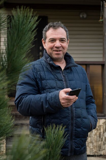 Un homme mûr en veste devant la maison.