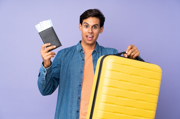 Homme sur mur violet isolé en vacances avec valise et passeport et surpris