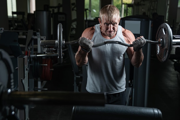 Homme musclé adulte brutal avec une barre pompe ses bras dans la salle de gym