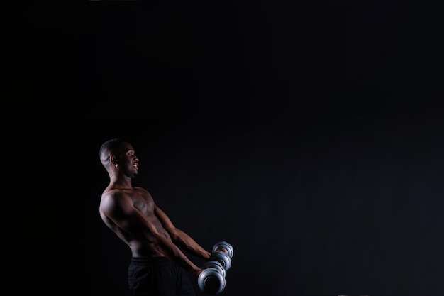 Photo homme musclé africain isolé avec des haltères sur fond de studio sombre fort mec noir torse nu