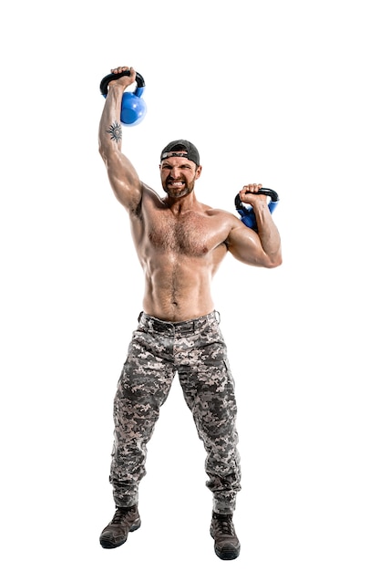 Homme musclé athlète bodybuilder en pantalon de camouflage avec un entraînement torse nu avec kettlebell sur un mur blanc. Isoler