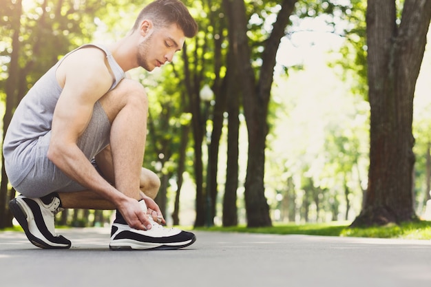 Homme musclé attachant des lacets sur des baskets avant de courir, se préparer pour faire du jogging dans le parc, gros plan, espace de copie, culture