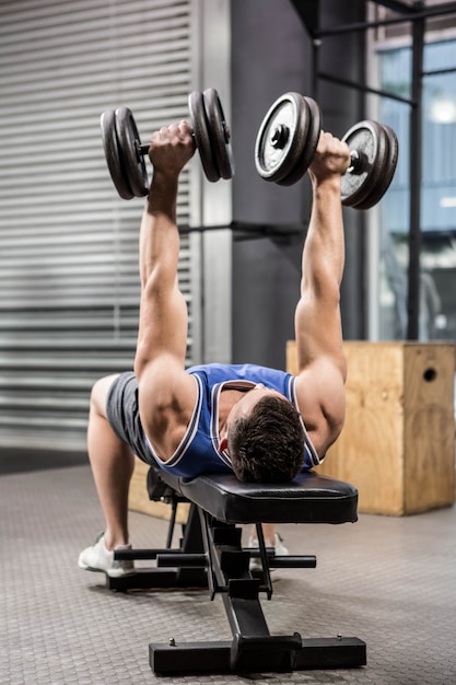 Homme musclé sur un banc soulevant des haltères au gymnase de crossfit