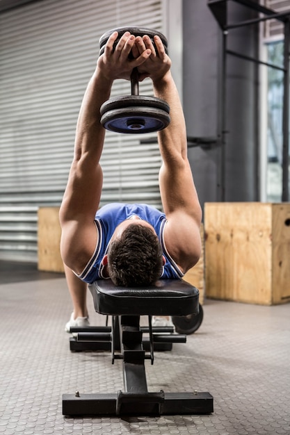 Homme musclé sur un banc, soulevant des haltères au gymnase de crossfit