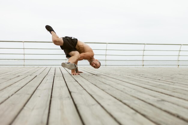 L'homme musclé bodybuilder se tient dans ses bras sur la plage.