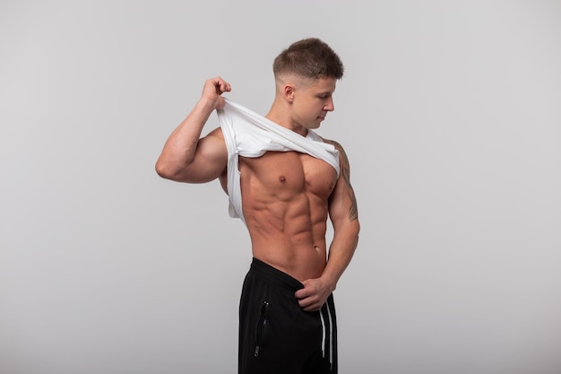 Homme musclé et en bonne santé en T-shirt blanc montrant des muscles abdominaux sur fond gris en studio Style de vie sportif