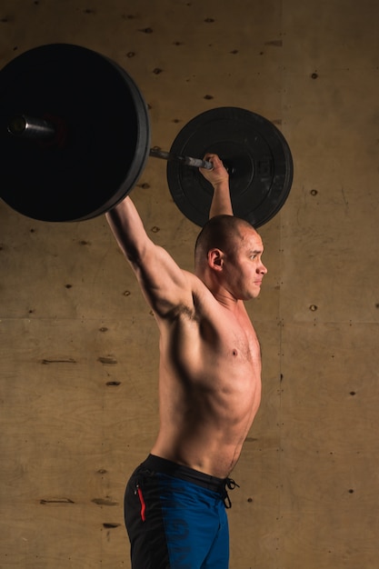 Homme musclé brutal avec barbe train avec haltères soulevées au-dessus de la tête dans la salle de gym