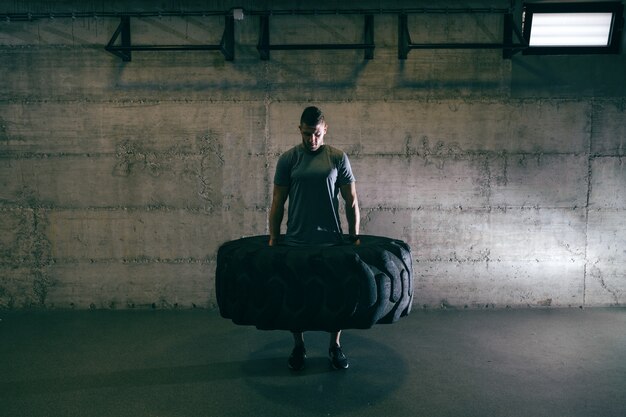 Homme musclé caucasien, levage de pneu sur sa formation cross-fit.