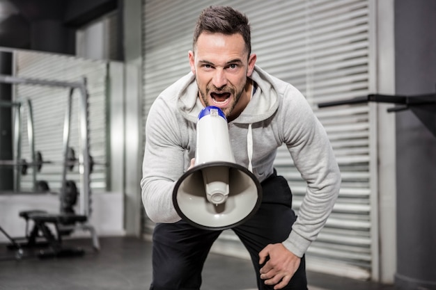 Homme musclé criant sur un mégaphone à la salle de gym crossfit