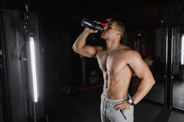 Homme musclé dans la salle de gym avec shaker. Abs masculins forts, arrière-plan concept de musculation. Bodybuilder dans la salle de gym.