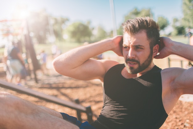 Homme musclé exerçant faisant de l'exercice assis. Athlète avec six pack, homme blanc, entraînement en plein air. Sports et mode de vie sain. Mec barbu aux cheveux noirs faisant des craquements à l'extérieur.