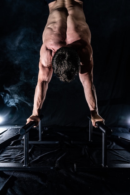 Homme musclé faisant du crossfit sur barre parallèle à l'intérieur sur fond noir fumé concept de mode de vie sain et de gymnastique suédoise