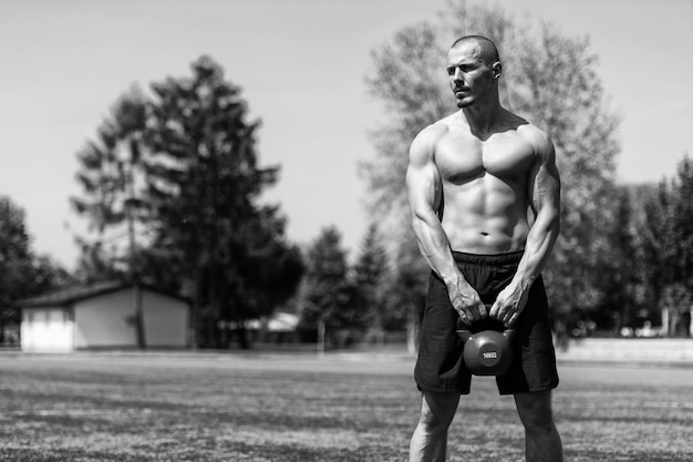 Homme musclé faisant de l'exercice avec Kettlebell en plein air