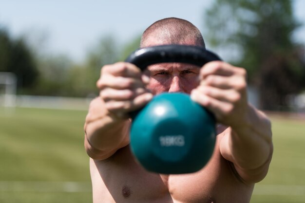 Homme musclé faisant de l'exercice avec Kettlebell en plein air