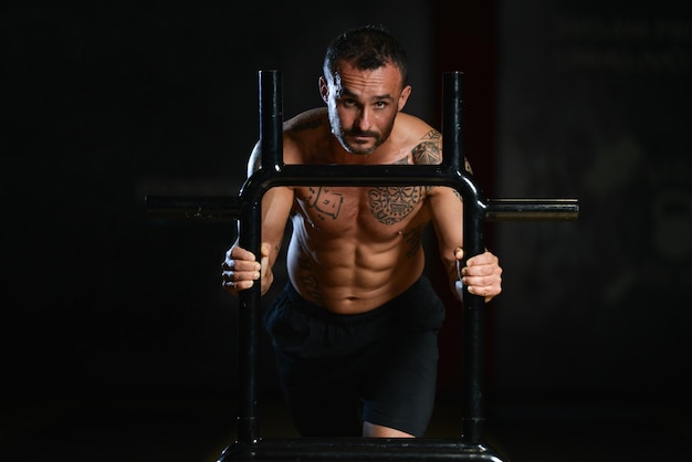 Homme musclé faisant de l'exercice de poids lourd Traîneau de vitesse pondérée dans la salle de sport