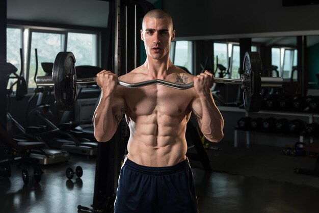 Homme musclé faisant des exercices de poids lourds pour les biceps avec des haltères dans la salle de sport