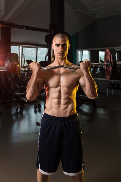 Homme musclé faisant des exercices de poids lourds pour les biceps avec des haltères dans la salle de sport