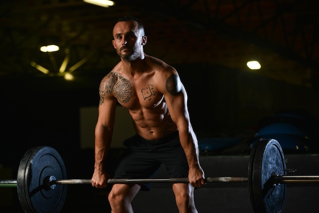 Homme musclé faisant des exercices de poids lourds pour le dos avec des haltères dans la salle de sport