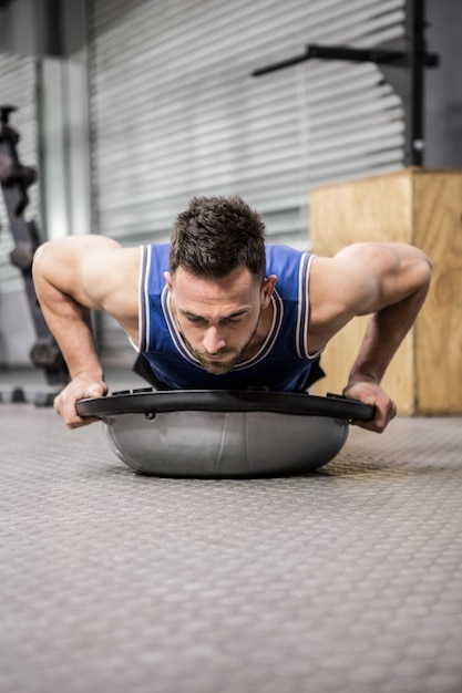 Homme musclé faisant pousser sur une balle de bosu au gymnase de crossfit