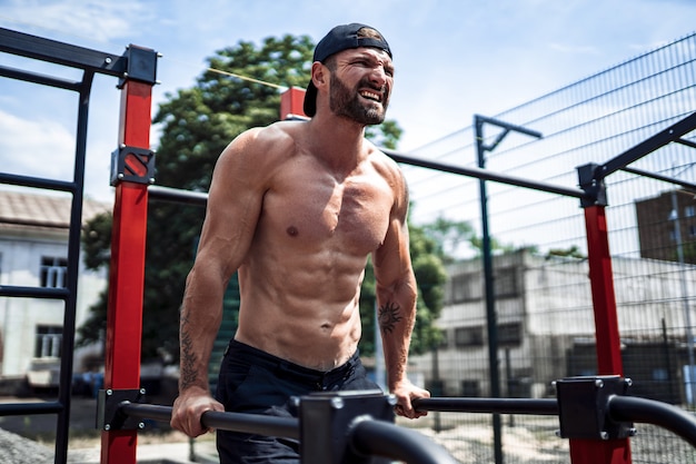 Homme musclé fort faisant des pompes sur des barres inégales dans une salle de sport de rue en plein air