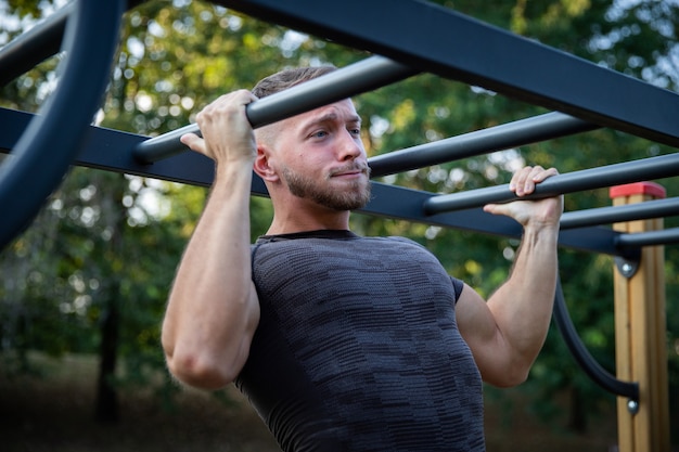 Homme musclé fort fait quelques tractions lors d'une séance d'entraînement en plein air dans le parc et exprime l'effort Grimace