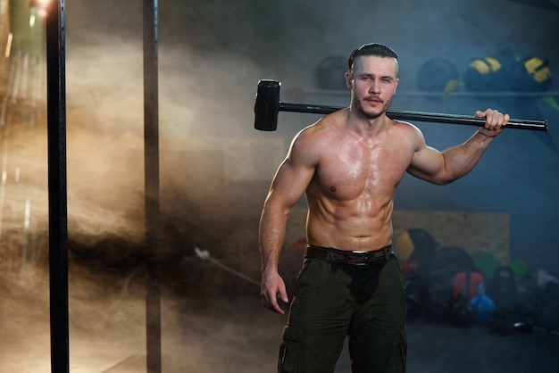 Homme musclé fort avec un marteau sur l'épaule.