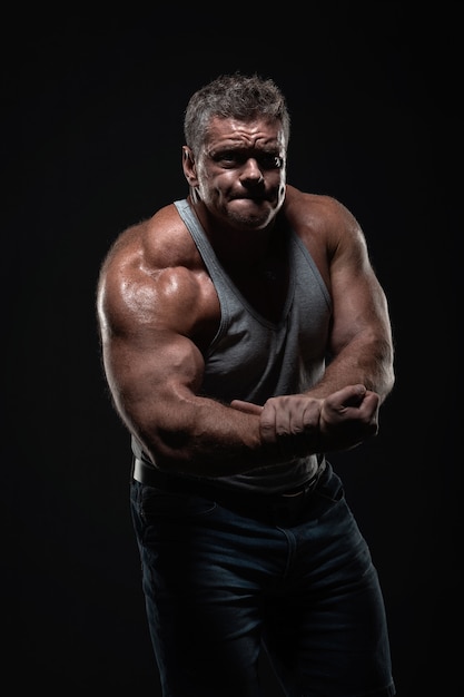 Homme musclé puissant montre les biceps sur fond noir. Concept de force et de fitness